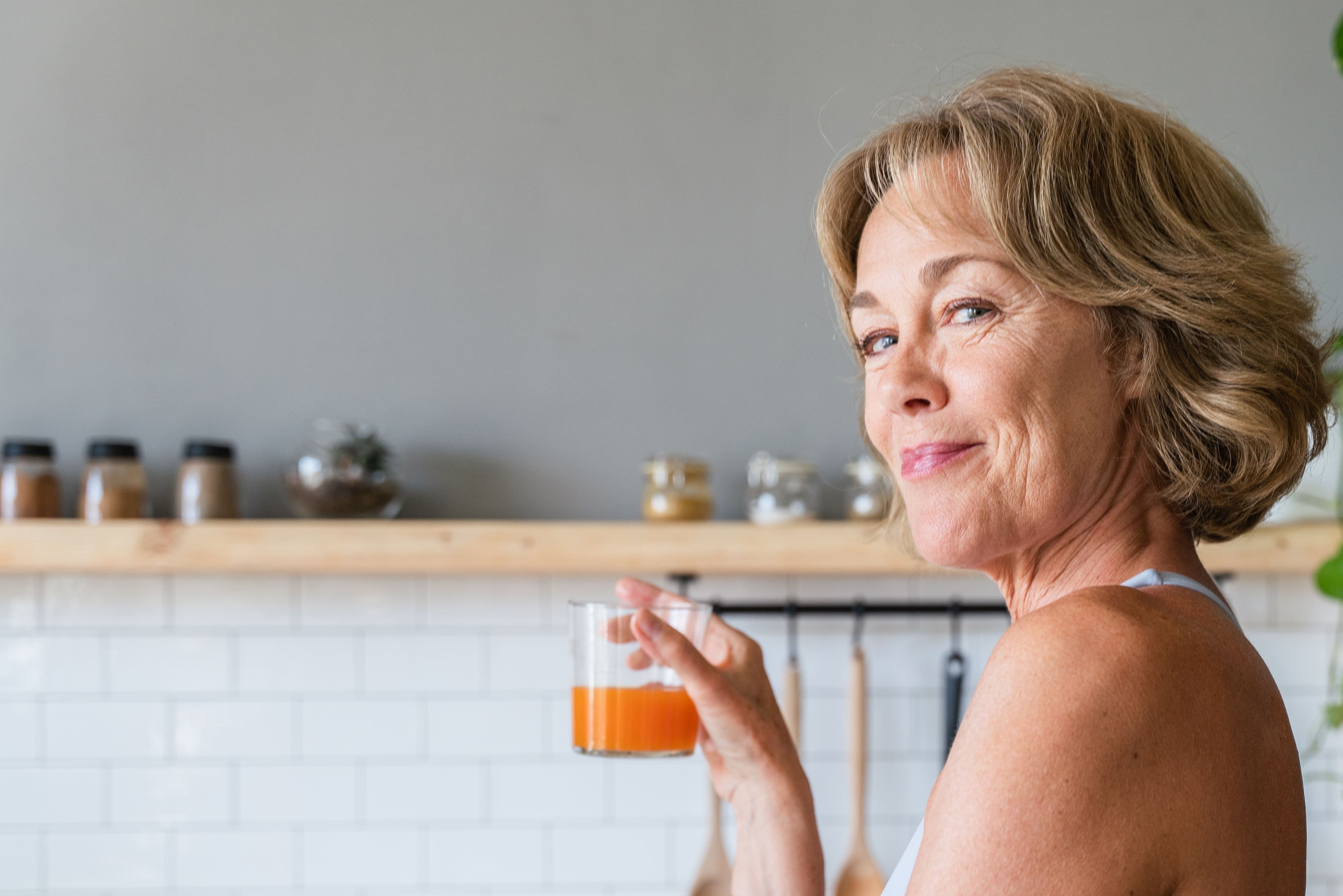 Mulher de meia idade segurando um copo de suco com colágeno Rejuv